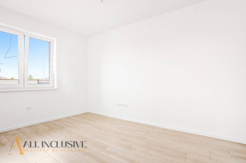 Üres szoba fehér falakkal és fa dekorációjú padlóval egy háromszobás lakásban.