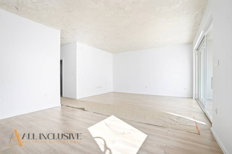 Tágas szoba világos falakkal, fa dekorációjú padló, 3 szobás lakás.