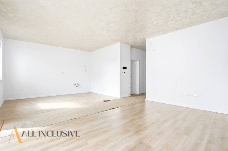 Tágas szoba fehér falakkal és fa dekorációjú padlóval egy háromszobás lakásban.