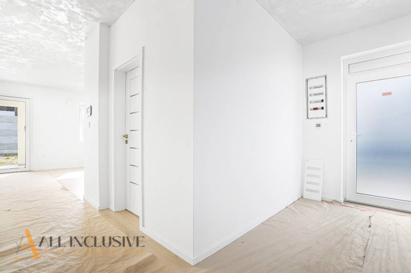 Világos folyosó egy háromszobás lakásban fehér falakkal és fa dekorációjú padlóval.