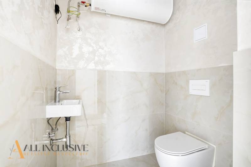 Fürdőszoba WC-vel és mosdóval egy háromszobás lakásban, világos csempe, víztartály.