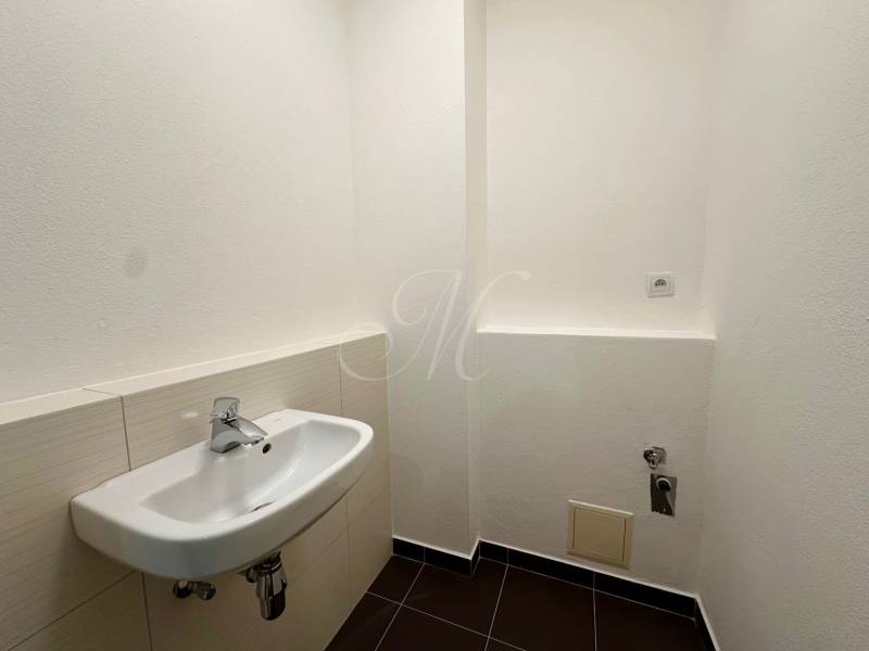 WC a négy szobás lakásban fehér mosdóval és fekete csempével.
