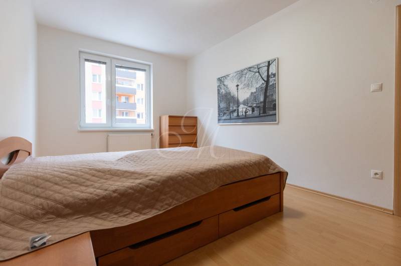 Hálószoba egy kétszobás lakásban beépített ággyal és képpel a falon.