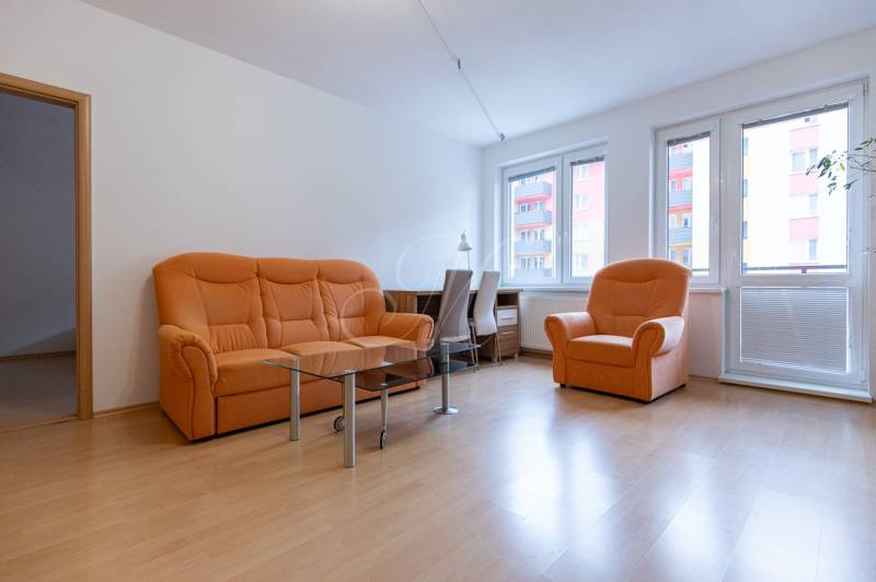 Nappali narancssárga kanapéval és fa dekorációjú padlóval egy kétszobás lakásban.