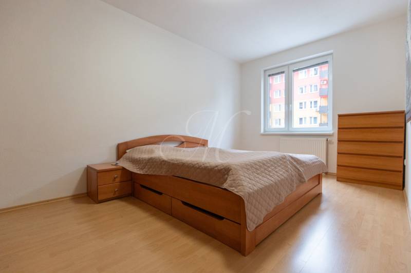 Világos falú szoba, franciaággyal és fa mintázatú padlóval egy kétszobás lakásban.