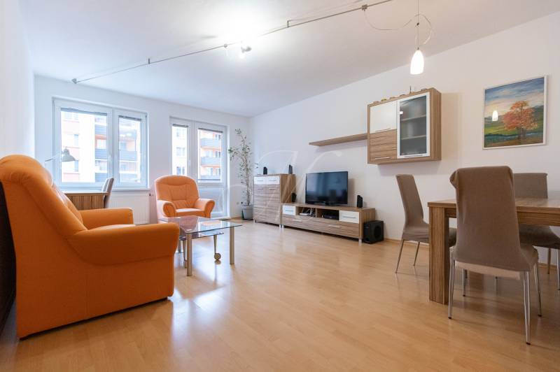 Nappali egy kétszobás lakásban narancssárga fotelekkel és fa mintázatú padlóval.