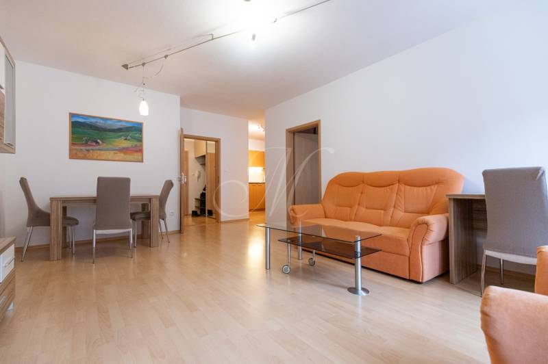 Nappali egy kétszobás lakásban narancssárga kanapéval és fa mintázatú padlóval.