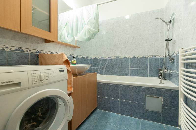 Fürdőszoba egy kétszobás lakásban mosógéppel, káddal és kék csempékkel.
