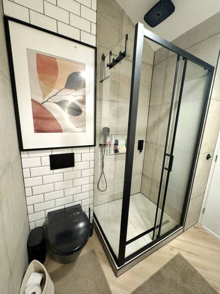 Fürdőszoba egy háromszobás lakásban üveg zuhanykabinnal és fekete WC-vel.