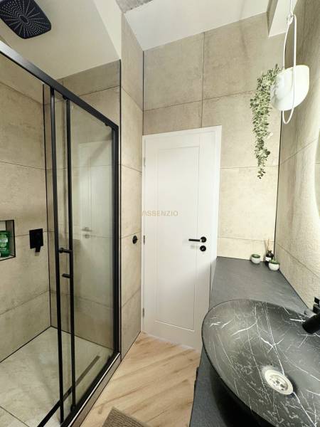 Fürdőszoba egy háromszobás lakásban fekete mosdóval, zuhanyzóval és fa mintázatú padlóval.