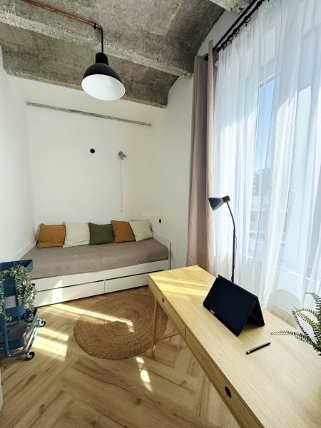 Szoba egy háromszobás lakásban fa dekorációval, ággyal és íróasztallal, amelyen egy tablet található.