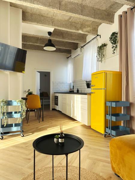 3 szobás lakás belső tere fa mintás padlóval, sárga hűtőszekrénnyel és fehér konyhabútorral.