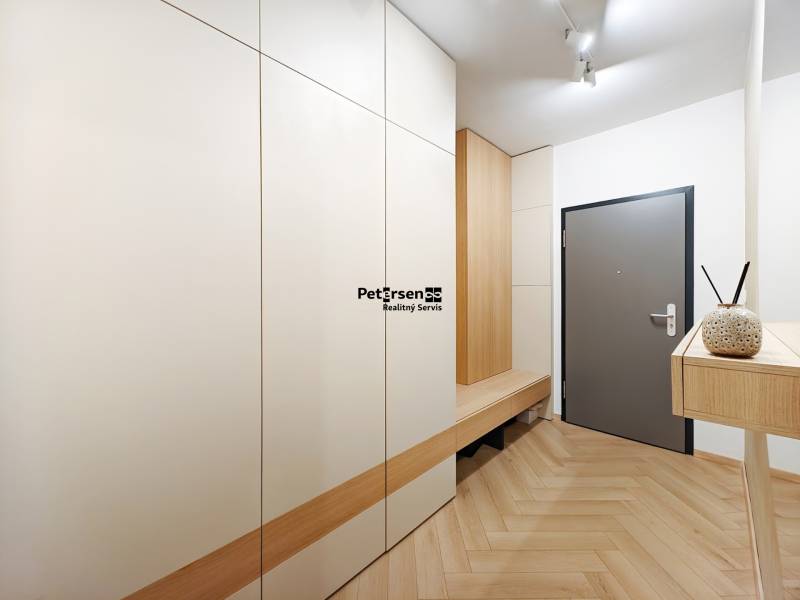 Bejárati folyosó fa mintázatú padlóval egy kétszobás lakásban fehér szekrényekkel.