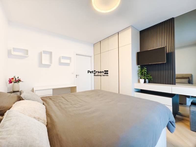 Hálószoba egy kétszobás lakásban ággyal, ruhásszekrénnyel és falra szerelt televízióval.