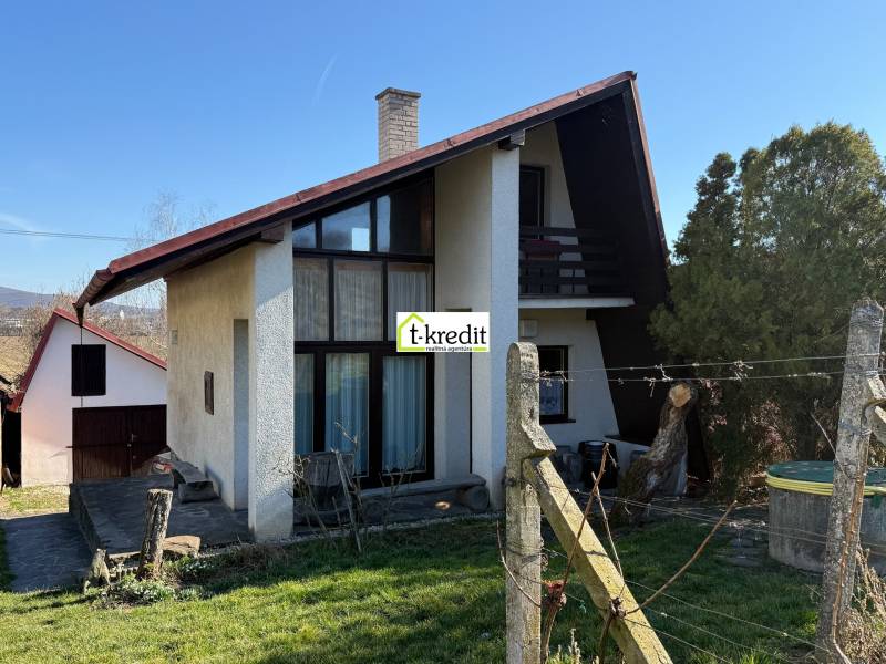 Házikó Aranyosmaróton fa kerítéssel, gyepes udvarral és körülötte fákkal.