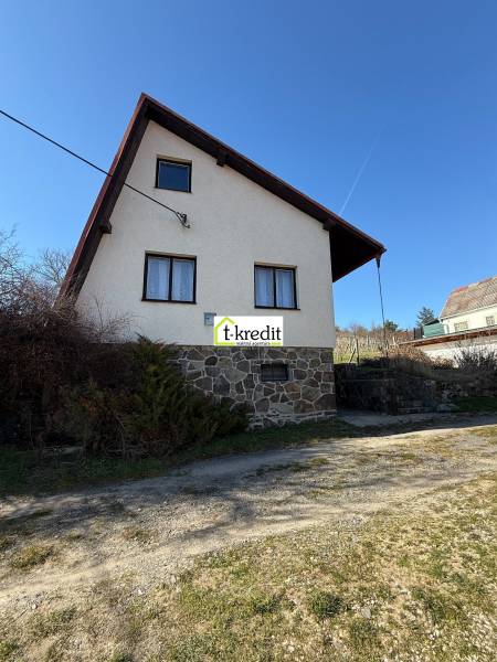 Kunyhó Aranyosmaróton kőalappal és ferde tetővel a kék ég alatt.