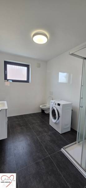 Fürdőszoba egy háromszobás lakásban zuhanyzóval, mosógéppel és fekete csempével.