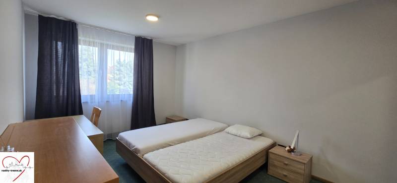 Hálószoba két ággyal, íróasztallal és ablakkal egy háromszobás lakásban.