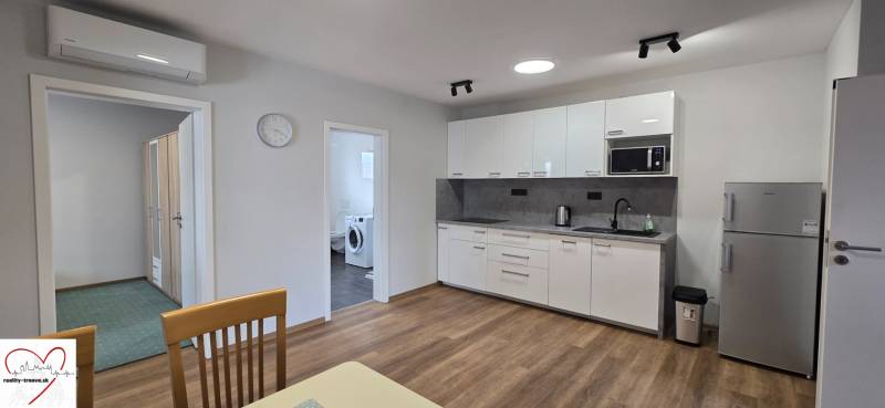 Konyha fehér szekrényekkel és készülékekkel egy háromszobás lakásban, fa dekor padlóval.