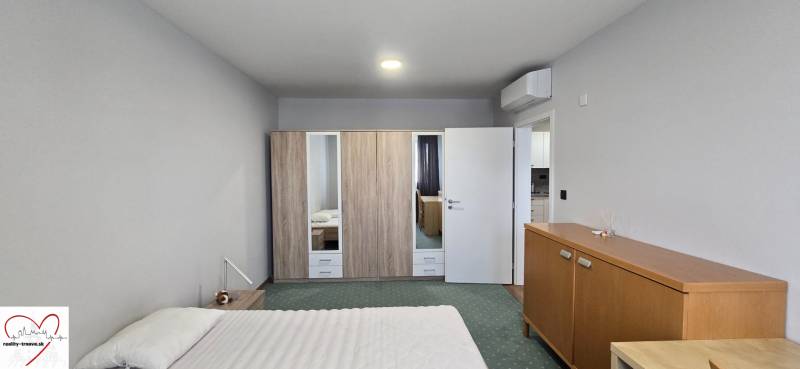 Szoba egy háromszobás lakásban ággyal, szekrénnyel, légkondicionálóval és fa dekorációjú bútorokkal.