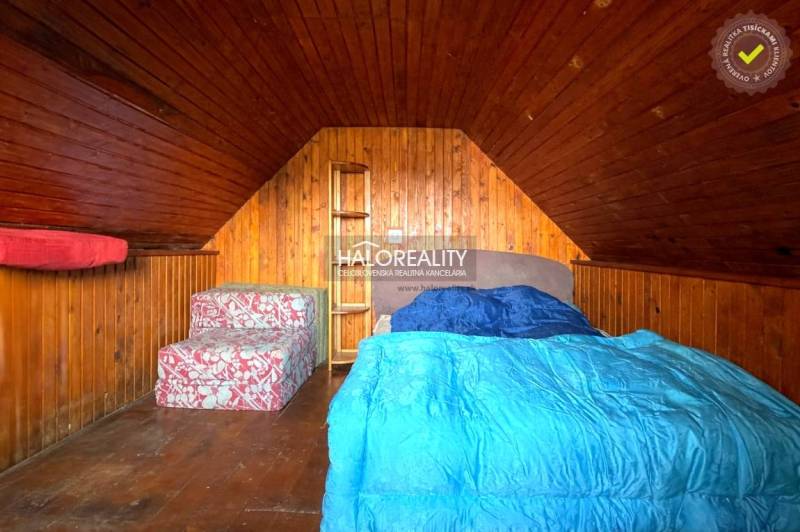 Padlásszoba fa burkolattal, ággyal és ülőgarnitúrával a házikóban.