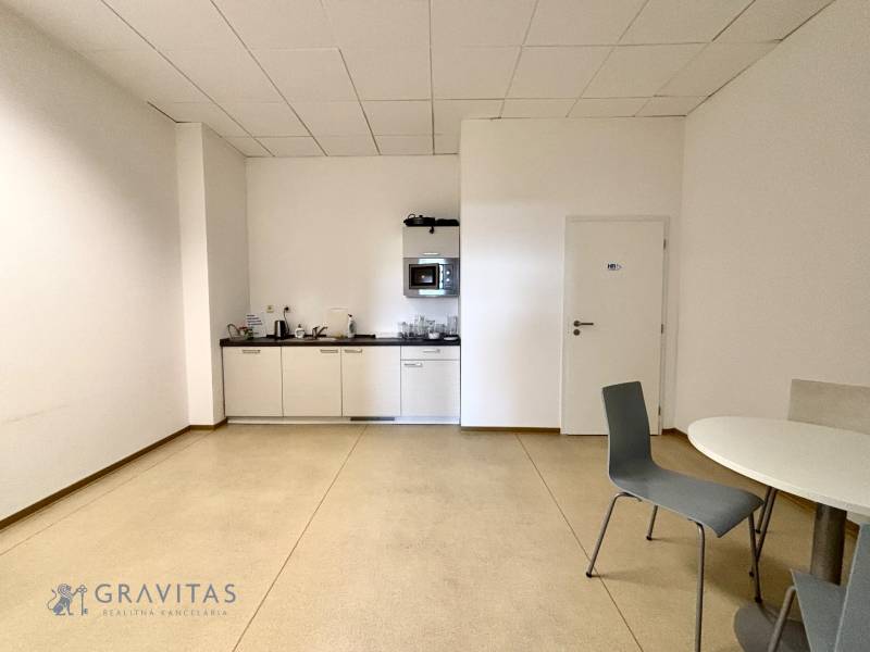 Irodai helyiségek konyhával, fehér szekrényekkel és szürke székekkel.