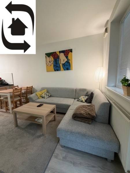 Világos nappali sarokkanapéval és művészettel egy kétszobás lakásban.