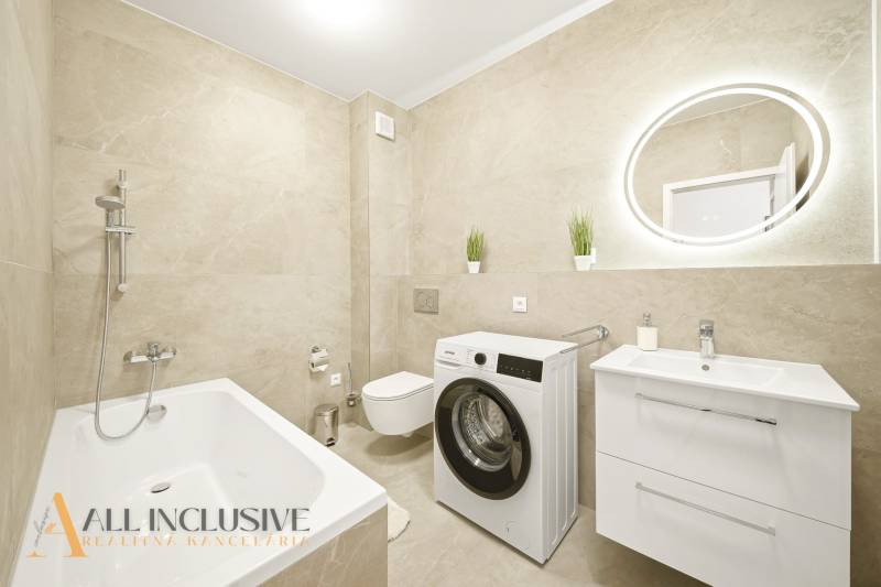 Fürdőszoba zuhanyzóval, mosógéppel és mosdóval egy négy szobás lakásban bézs csempével.