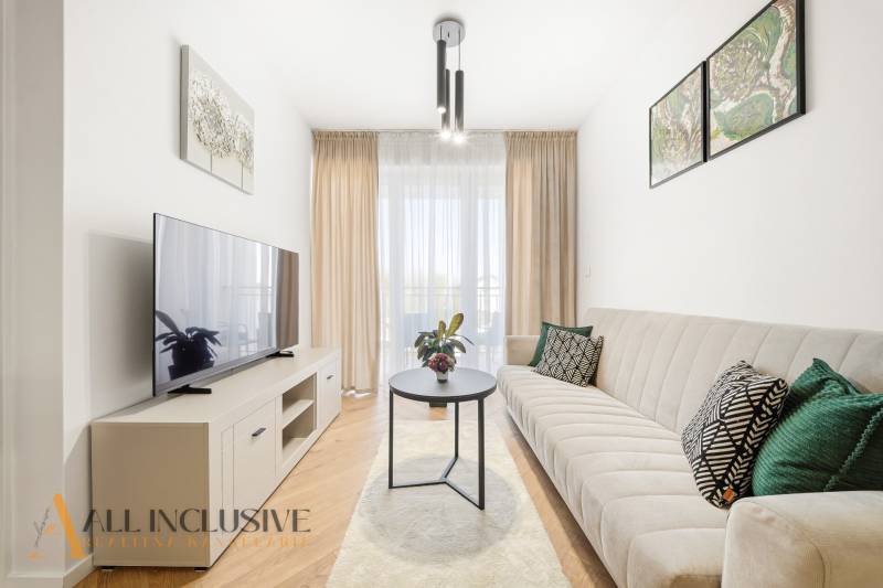 Nappali egy 4 szobás lakásban, fa mintázatú padlóval, világos bútorokkal és kanapéval.