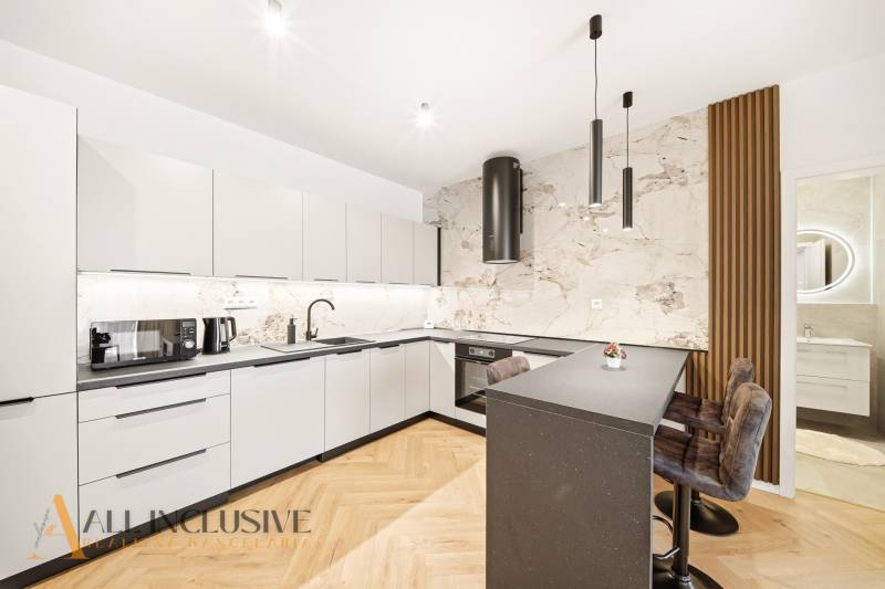 Konyha fehér szekrényekkel, szigettel és fa hatású padlóval egy 4 szobás lakásban.