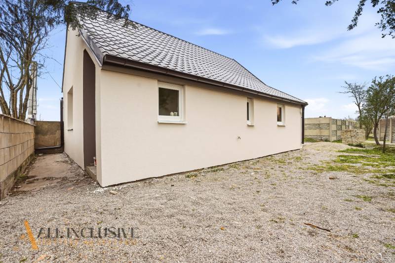 Családi ház Alsóvámoson fehér homlokzattal és ferde tetővel, köves telken.