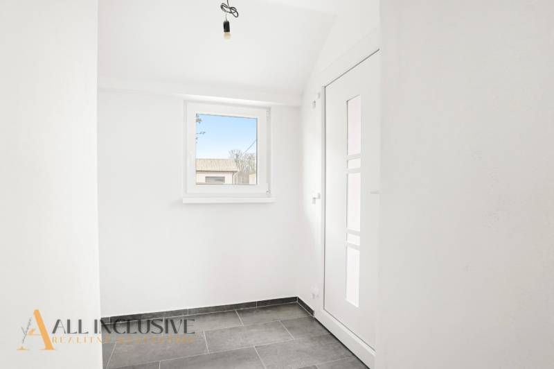 Családi ház előszobája ablakkal és világos falakkal, csempézett padlóval.