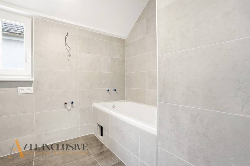 Fürdőszoba családi házban káddal és világos csempékkel a falakon.