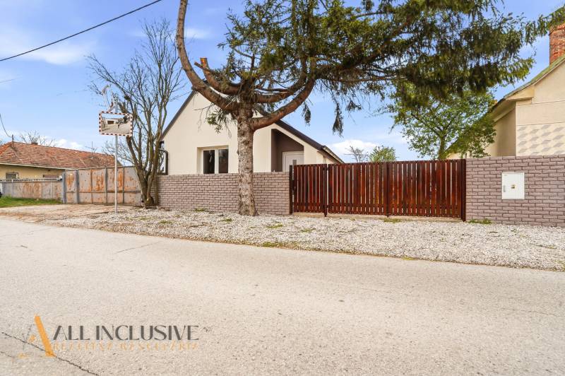 Családi ház Alistálon fallal és kapuval, fákkal és cementtel körülvéve.