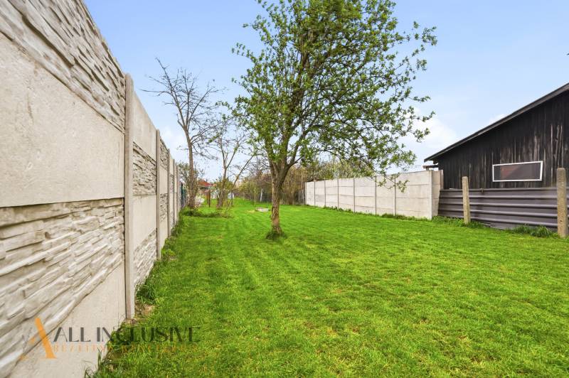 Kert pázsittal és fákkal a családi házban Dolný Bar-ban, a kerítés mentén.