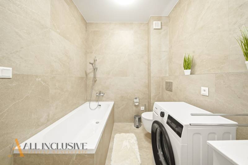 Világos csempékkel, káddal, mosógéppel és dekoratív növényekkel ellátott fürdőszoba egy négy szobás lakásban.