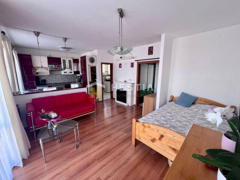 Nappali piros kanapéval, üvegasztallal és konyhával egy egyszobás lakásban.