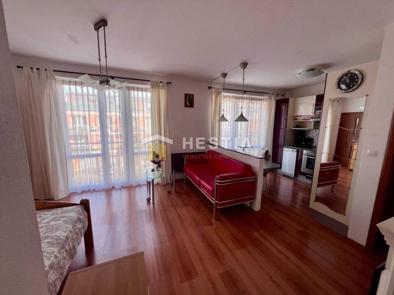 Egy szobás lakás belső tere fa padlóval, konyhával, világos függönyökkel és kényelmes ülőhellyel.