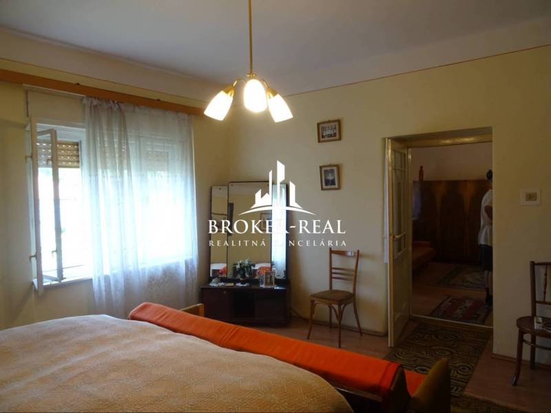 Hálószoba családi házban fa dekor padlóval, ágy, fotel, székek.