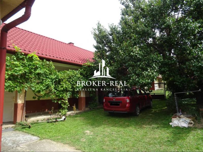 A Goncruszkei családi ház kertje piros tetővel és autóval a gyepen.