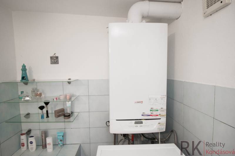 Fürdőszoba gázkazánnal és kozmetikai polcokkal a családi házban.