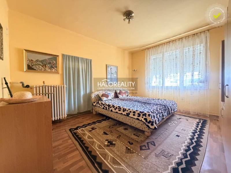 Hálószoba családi házban, fa dekoros padlóval, nagy ablakkal és szőnyegekkel.