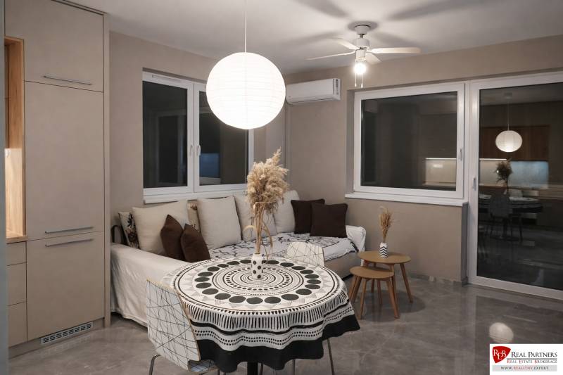 Nappali kanapéval, kerek asztallal és díszes lámpával egy kétszobás lakásban.