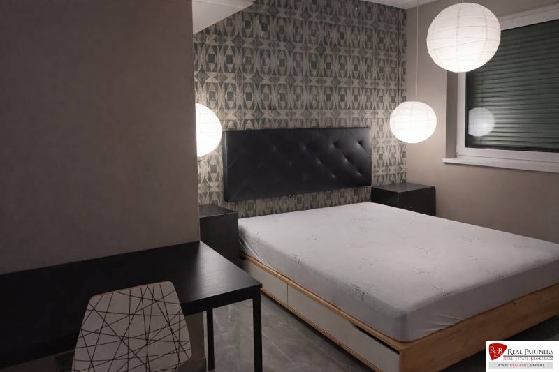 Hálószoba ággyal, esti világítás, asztal és szék egy kétszobás lakásban.