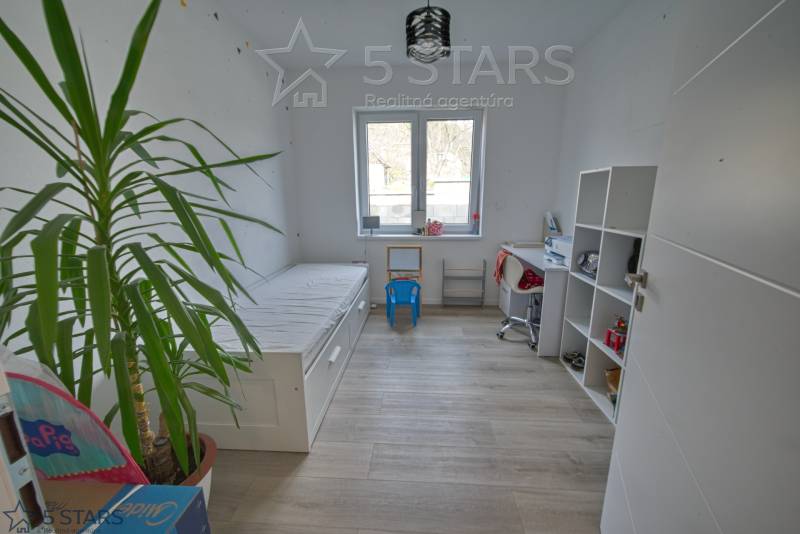 Gyerekszoba családi házban ággyal, asztallal és polccal, fa dekorációval ellátott padlón.