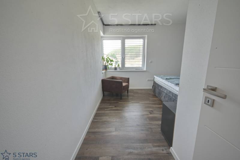 Szoba egy családi házban fa dekorációjú padlóval, székkel és ablakkal.