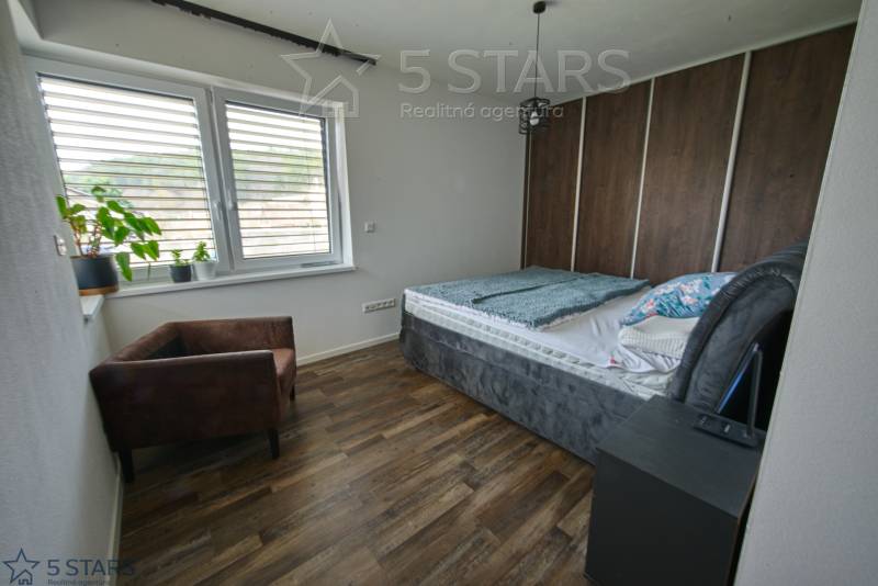 Hálószoba családi házban ággyal, székkel és fa mintázatú padlóval.