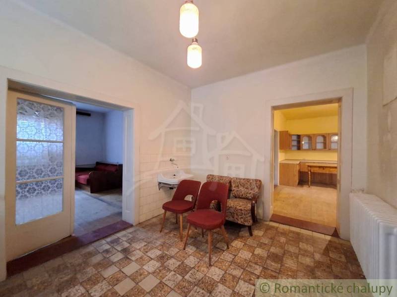 Családi ház belső tere fotelekkel, mosdóval, konyhával és két nyitott ajtóval.