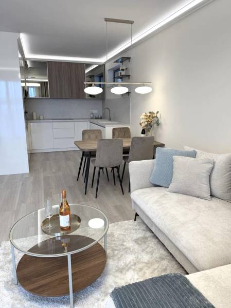 Nappali egy kétszobás lakásban, fa mintázatú padlóval, kanapéval és étkezőasztallal.