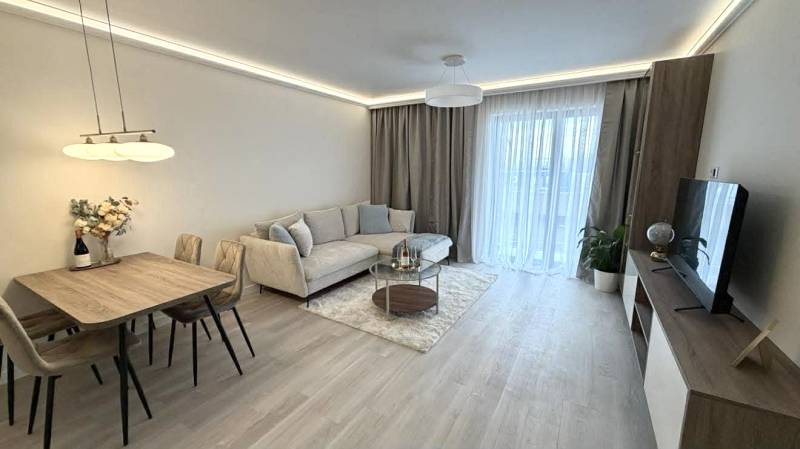 Nappali egy kétszobás lakásban, fa mintázatú padlóval, kanapéval és étkezőasztallal.